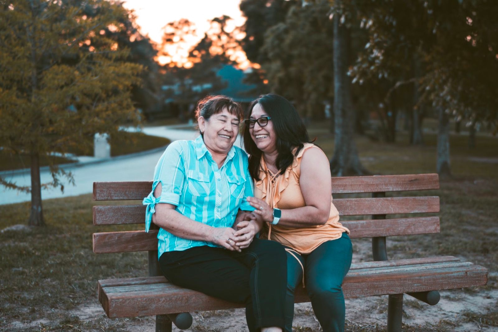 Dos mujeres riéndose juntas en una banca del parque al atardecer