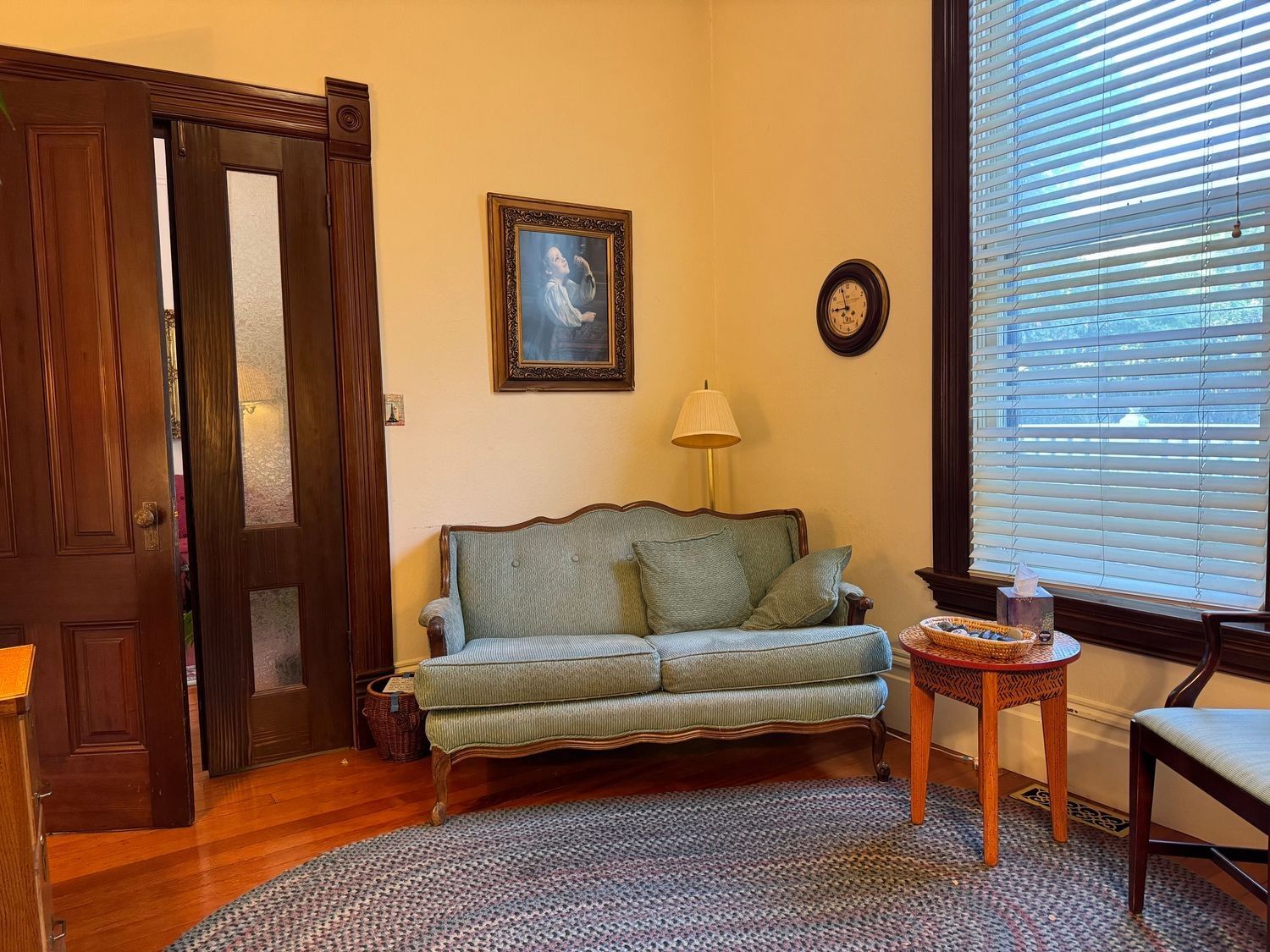 A sage-green loveseat beside a floor lamp and a tall window with blinds
