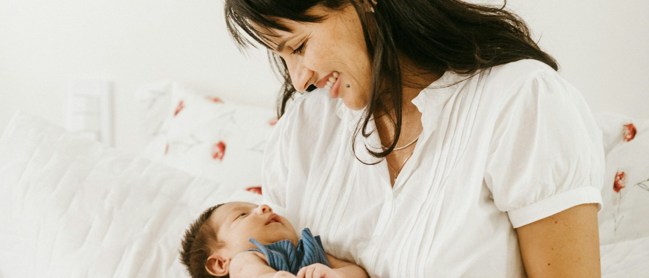 A mother sitting on a bed, smiling down at the newborn in her lap