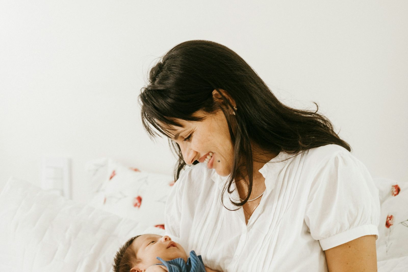A mother sitting on a bed, smiling down at the newborn in her lap
