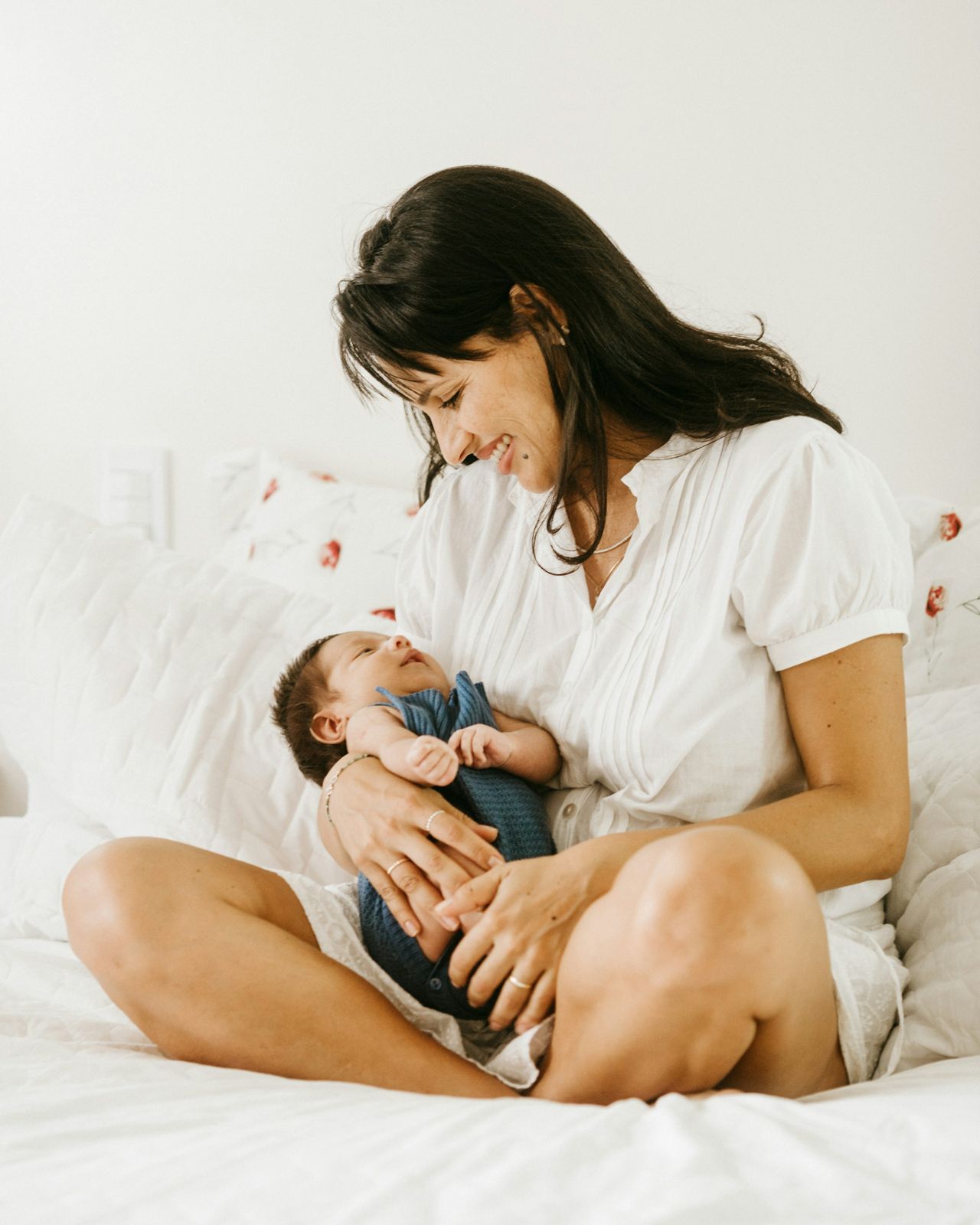 A mother sitting on a bed, smiling down at the newborn in her lap